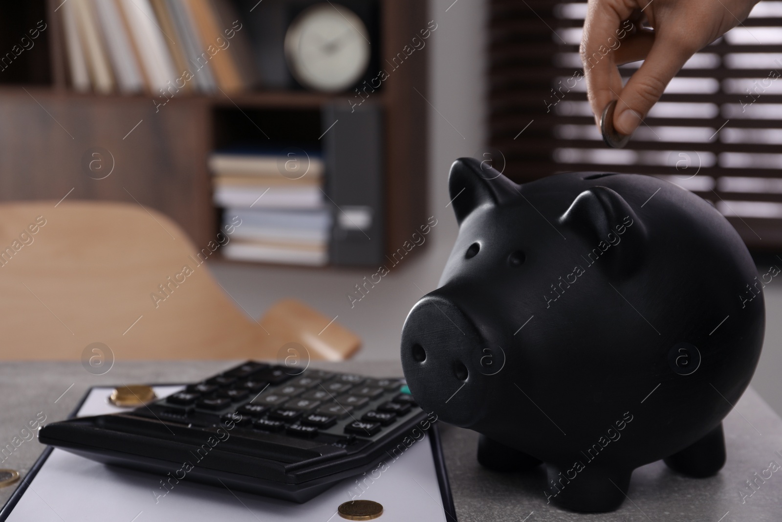 Photo of Woman putting coin into piggy bank at grey table indoors, closeup