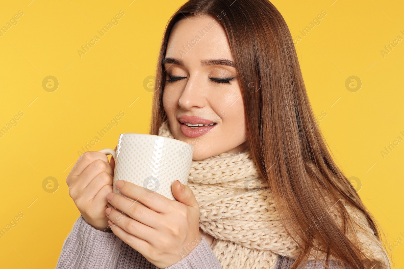 Photo of Beautiful young woman in sweater with drink on yellow background. Winter season