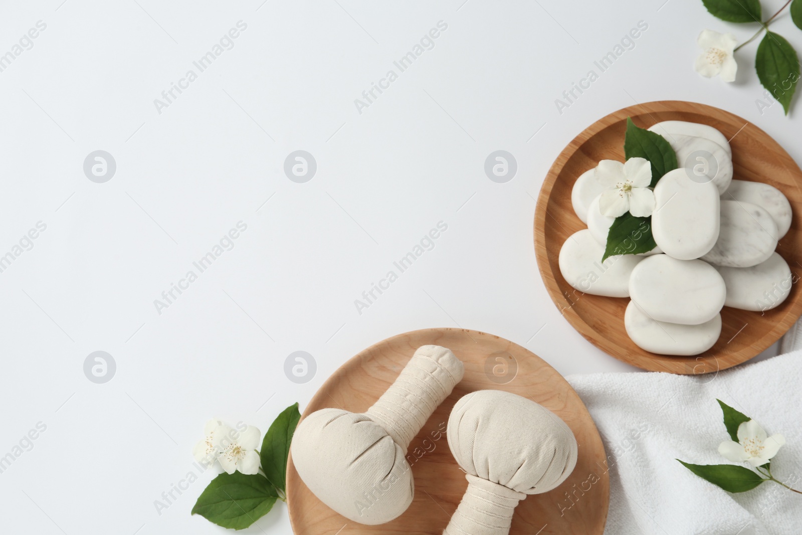 Photo of Spa stones, beautiful jasmine flowers, towel and herbal bags on white background, flat lay. Space for text