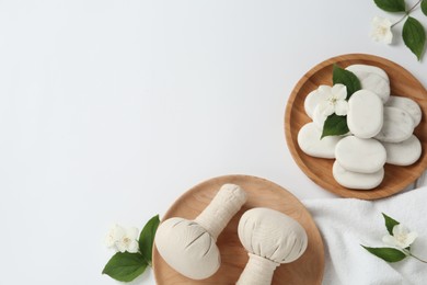 Spa stones, beautiful jasmine flowers, towel and herbal bags on white background, flat lay. Space for text