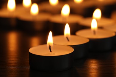 Burning tealight candles on dark surface, closeup