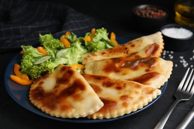 Photo of Delicious fried chebureki with vegetables served on black table