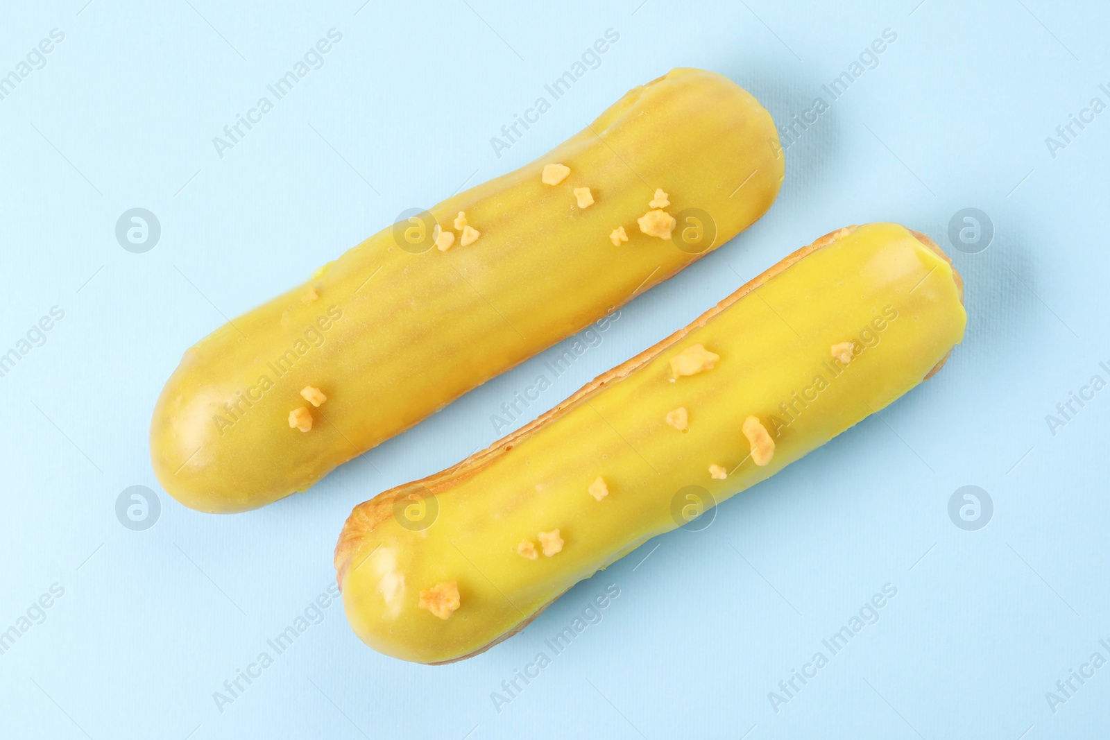 Photo of Delicious eclairs covered with glaze on light blue background, top view