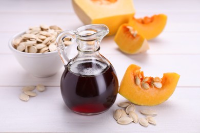 Photo of Fresh pumpkin seed oil in glass jug on white wooden table