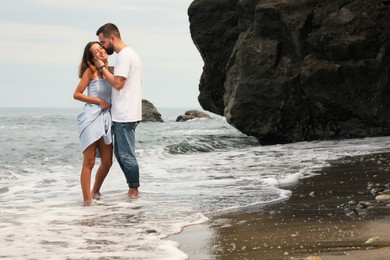 Photo of Happy young couple spending time together on beach near sea, space for text