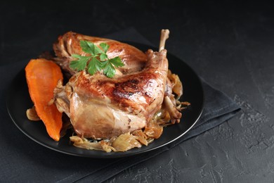 Photo of Tasty cooked rabbit meat with vegetables and parsley on black table, closeup. Space for text