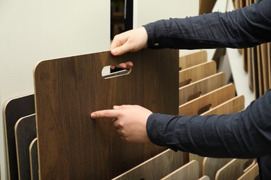 Photo of Man choosing wooden flooring among different samples in shop, closeup