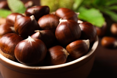 Photo of Fresh sweet edible chestnuts in bowl on table, closeup