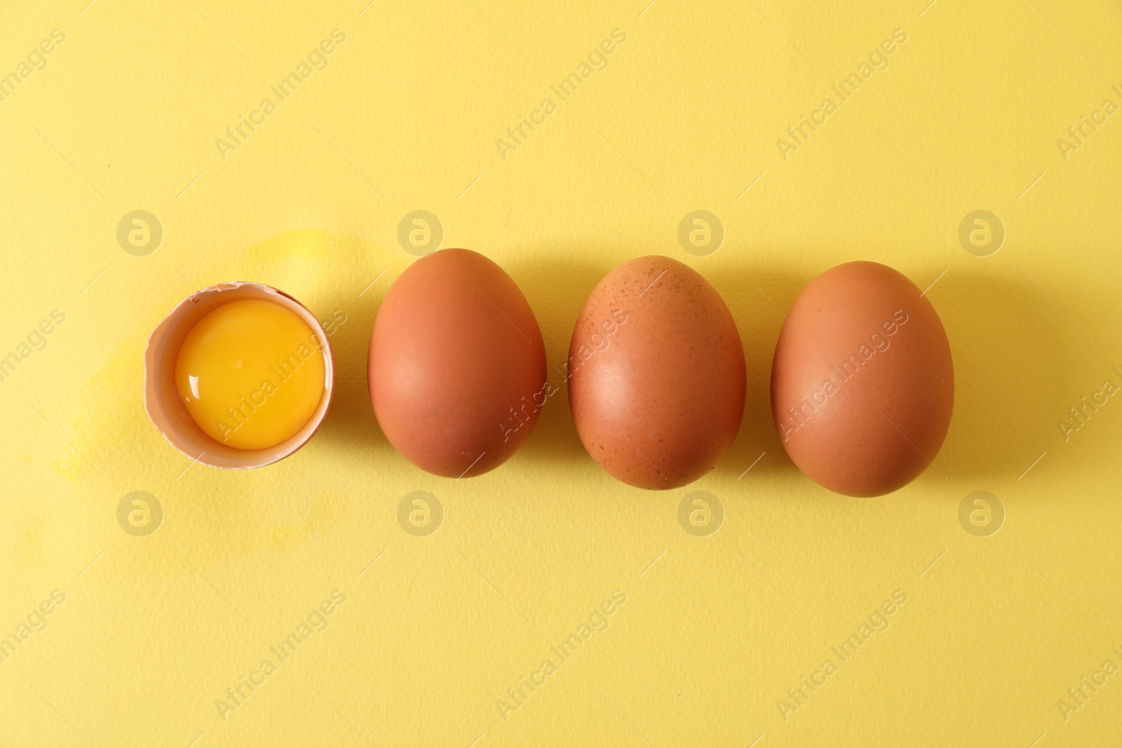 Photo of Cracked and whole chicken eggs on yellow background, flat lay