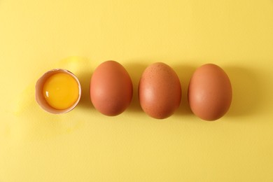 Cracked and whole chicken eggs on yellow background, flat lay