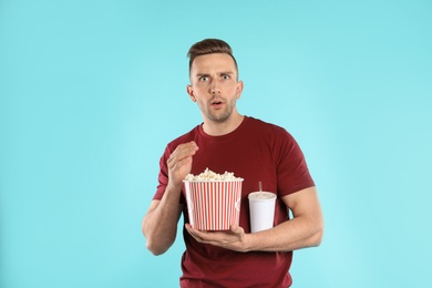 Emotional man with popcorn and beverage during cinema show on color background