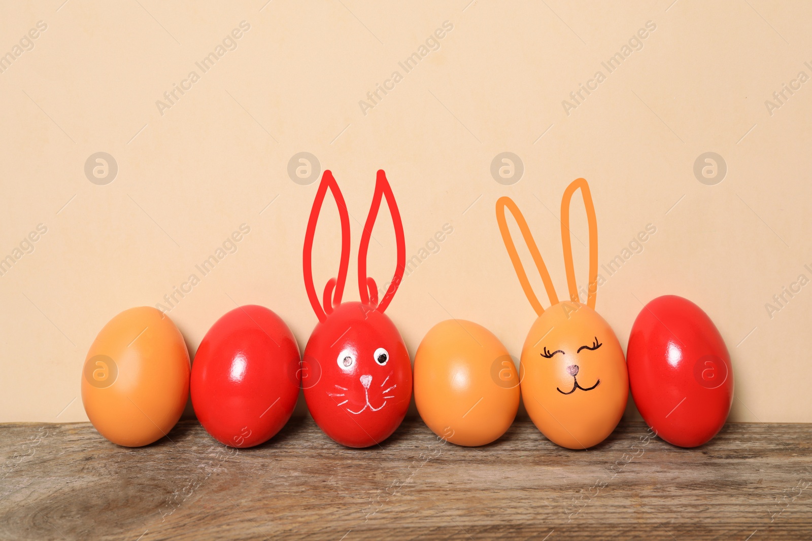 Image of Two eggs with drawn faces and ears as Easter bunnies among others on wooden table against beige background