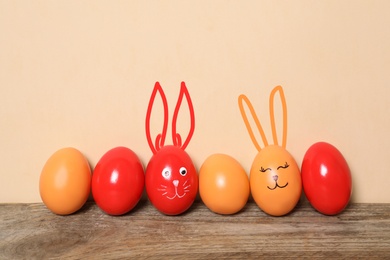 Image of Two eggs with drawn faces and ears as Easter bunnies among others on wooden table against beige background