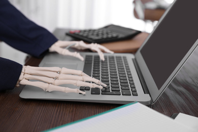 Photo of Human skeleton in suit using laptop at table, closeup