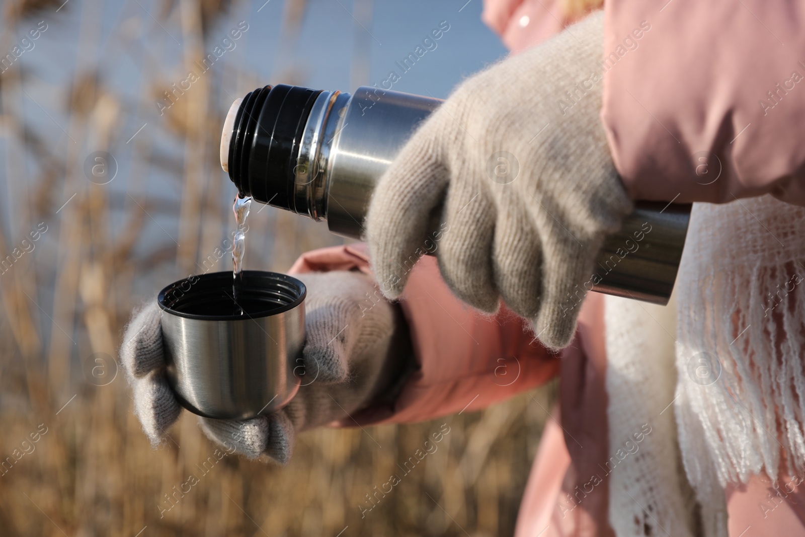 Photo of Woman pouring hot drink into cup from thermos outdoors, closeup