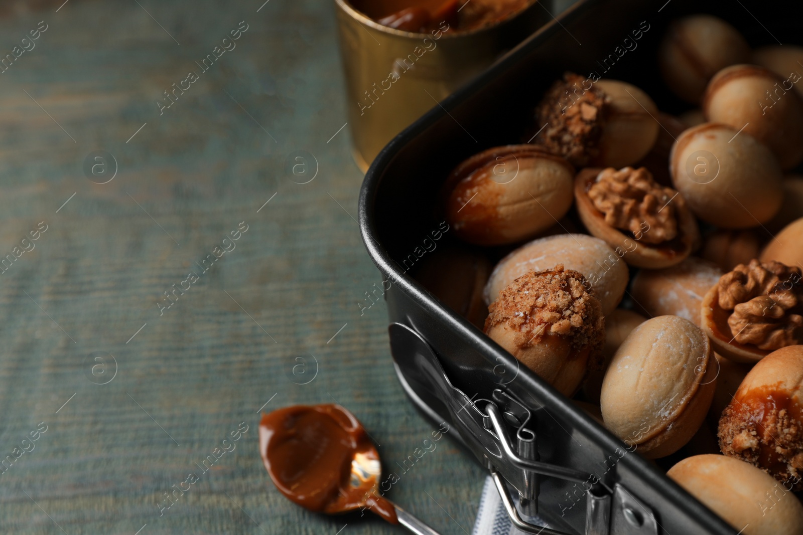 Photo of Freshly baked homemade walnut shaped cookies and boiled condensed milk on wooden table, closeup. Space for text