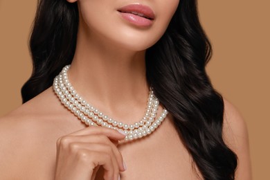 Photo of Young woman wearing elegant pearl necklace on brown background, closeup