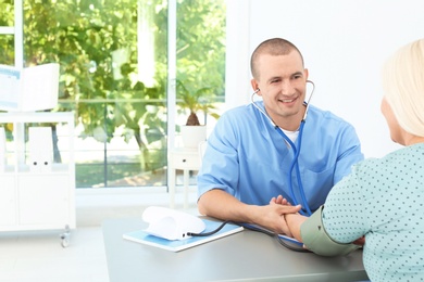 Male medical assistant measuring female patient blood pressure in clinic