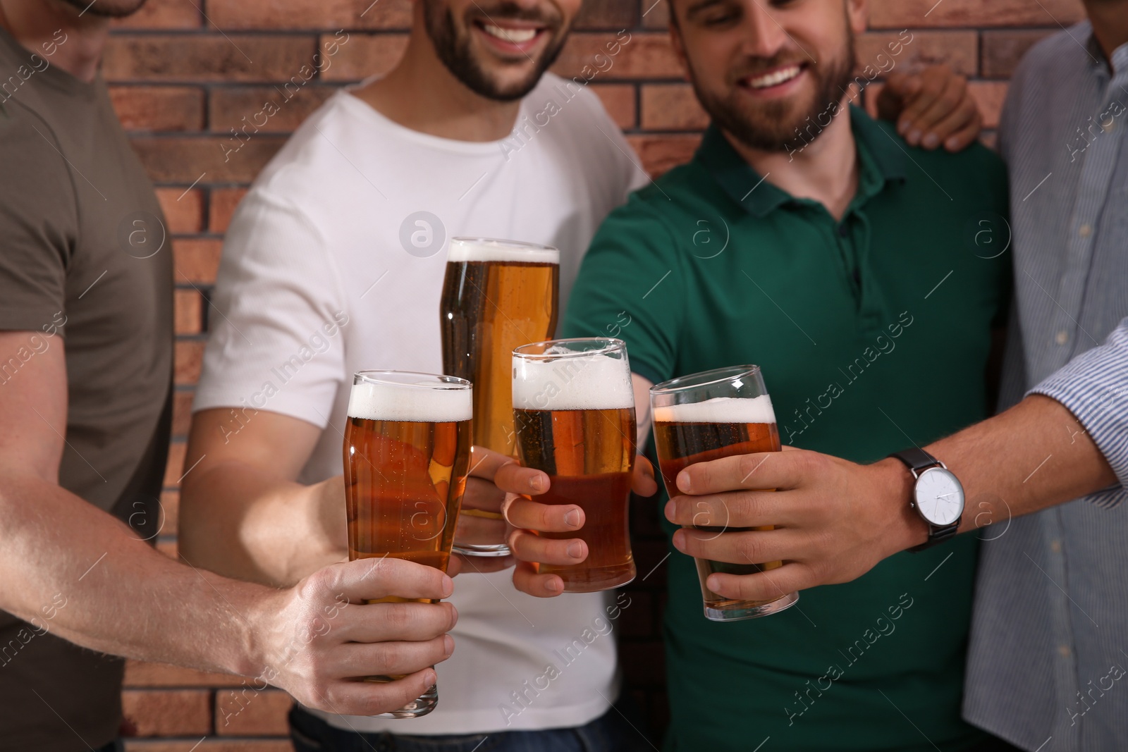 Photo of Friends clinking glasses of beer near red brick wall, closeup