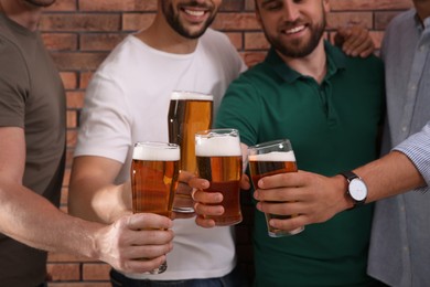 Friends clinking glasses of beer near red brick wall, closeup