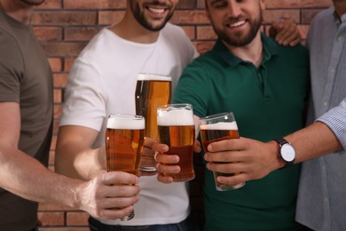 Photo of Friends clinking glasses of beer near red brick wall, closeup