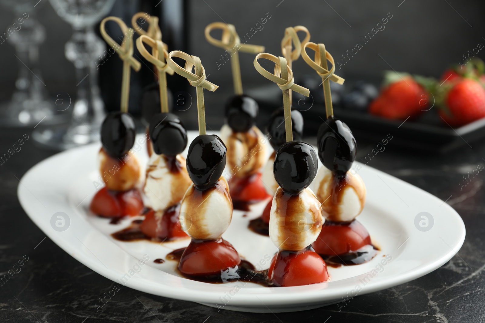 Photo of Tasty canapes with black olives, mozzarella and cherry tomatoes on dark textured table, closeup