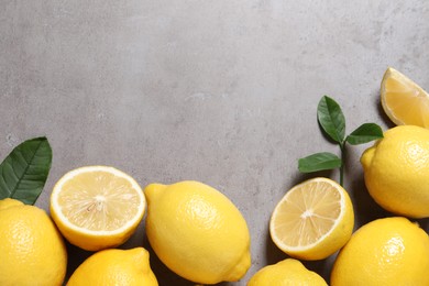 Fresh lemons and green leaves on grey table, flat lay. Space for text