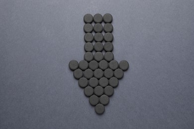 Photo of Arrow made of activated charcoal pills on grey background, flat lay. Potent sorbent
