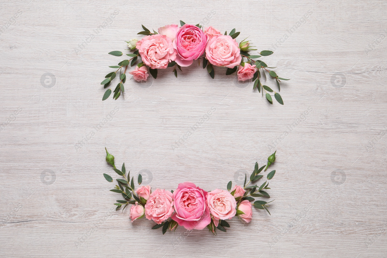 Photo of Wreath made of beautiful rose flowers and green leaves on white wooden background, flat lay. Space for text
