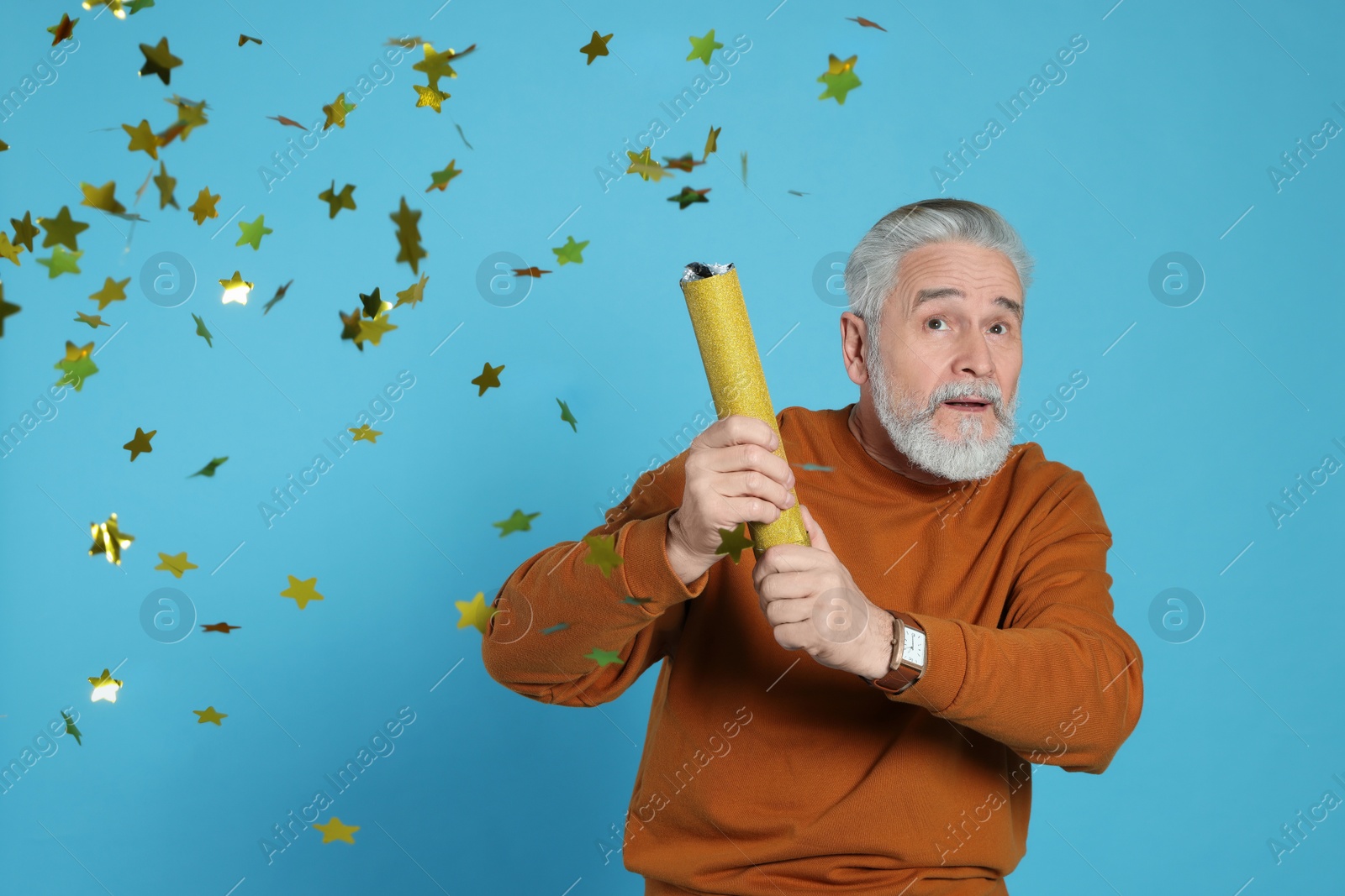 Photo of Emotional man blowing up party popper on light blue background