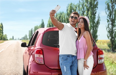 Happy young couple taking selfie near car on road