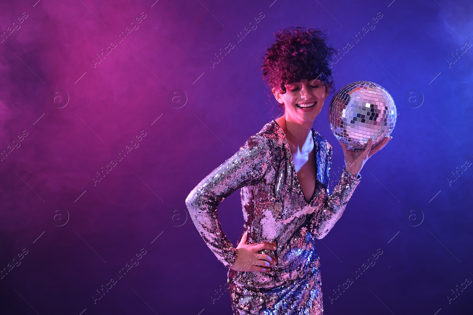 Photo of Beautiful young woman with disco ball posing on color background in neon lights. Space for text