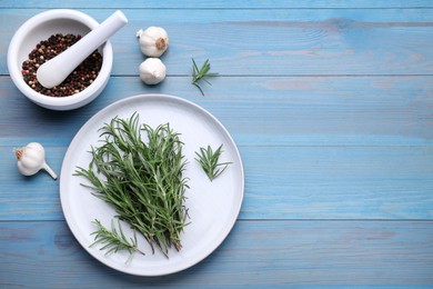 Rosemary, mortar and garlic on light blue wooden table, flat lay. Space for text