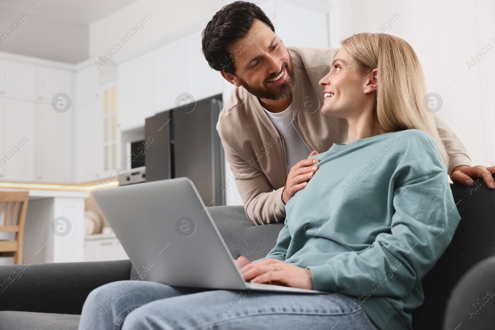 Photo of Happy couple using laptop on sofa at home, low angle view