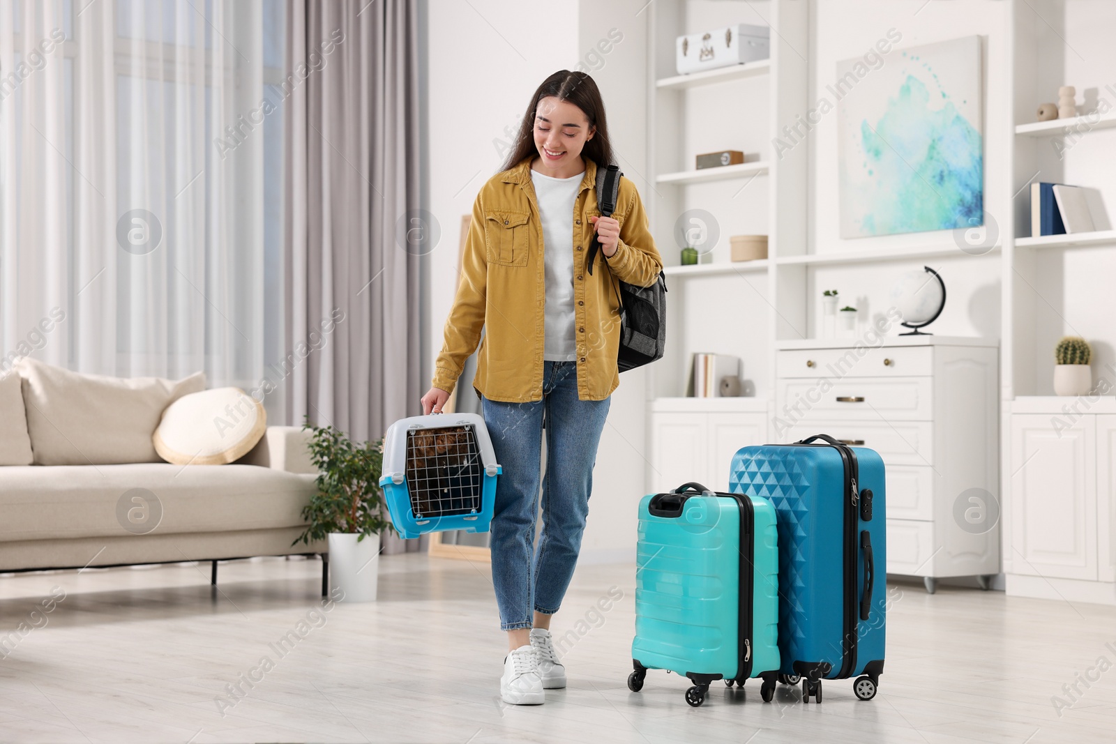 Photo of Travel with pet. Smiling woman with backpack holding carrier with dog at home