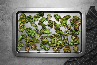 Tasty baked kale chips on grey table, top view