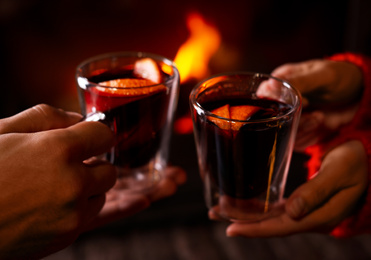 Photo of Couple with tasty mulled wine near fireplace indoors, closeup