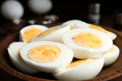 Photo of Cut hard boiled chicken eggs in wooden bowl, closeup