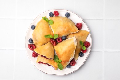 Plate of delicious samosas, berries and mint leaves on white tiled table, top view