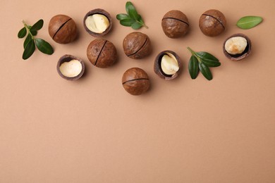 Tasty Macadamia nuts and green leaves on beige background, flat lay. Space for text