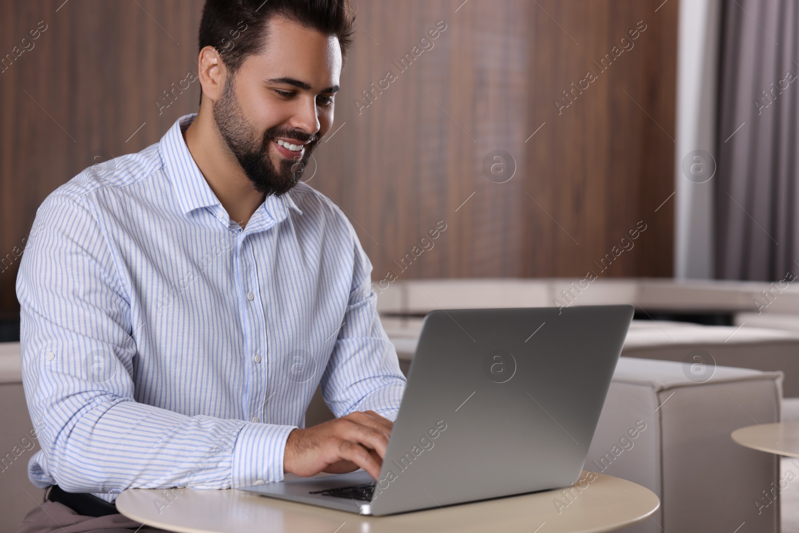 Photo of Happy young man working on laptop at table in office