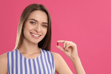 Young woman with vitamin pill on pink background