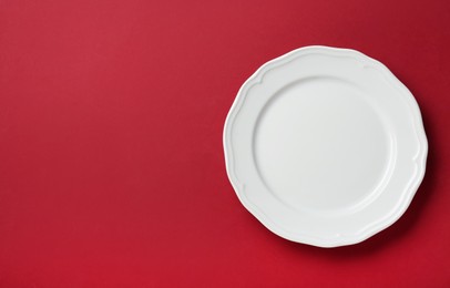 Photo of Clean white plate on red background, top view. Space for text