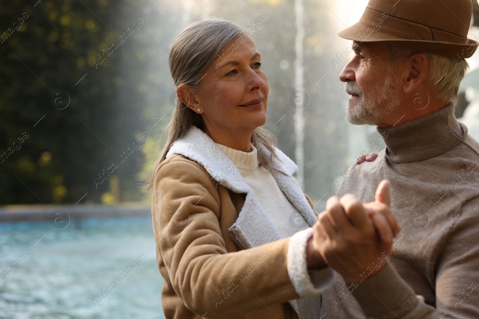 Photo of Affectionate senior couple dancing together near fountain outdoors, space for text