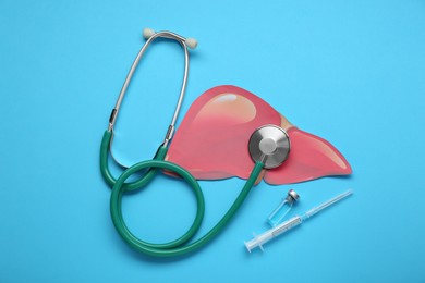 Photo of Paper liver, stethoscope, syringe and vial on light blue background, flat lay. Hepatitis treatment