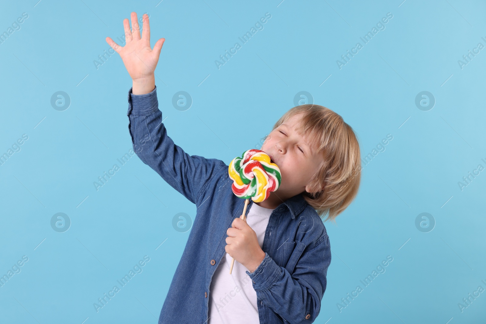 Photo of Cute little boy licking colorful lollipop swirl on light blue background