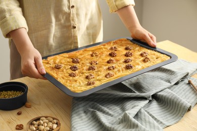 Woman holding baking pan of delicious baklava with walnuts above wooden table, closeup