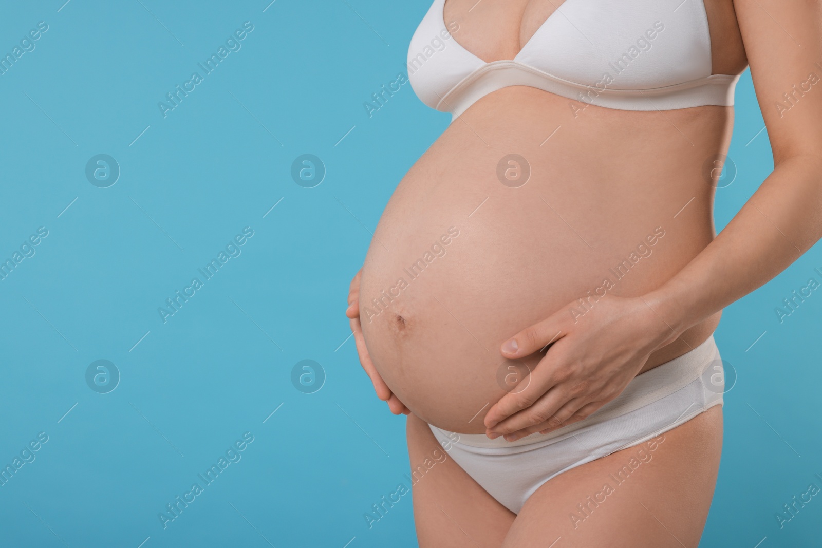 Photo of Pregnant woman in stylish comfortable underwear on light blue background, closeup. Space for text