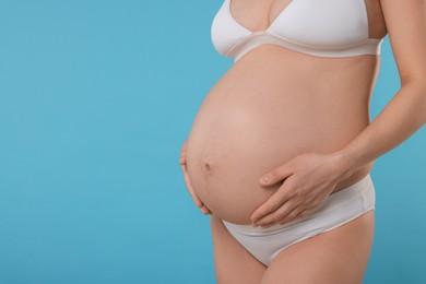 Pregnant woman in stylish comfortable underwear on light blue background, closeup. Space for text