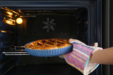 Woman taking delicious currant pie out of oven, closeup